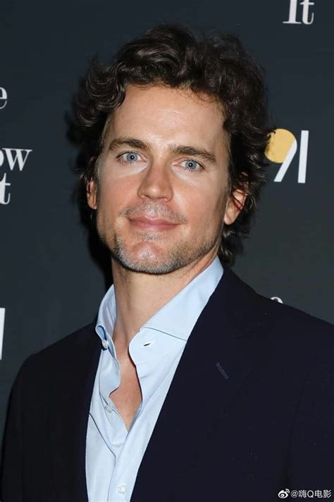 A Man With Curly Hair Wearing A Suit And Blue Shirt
