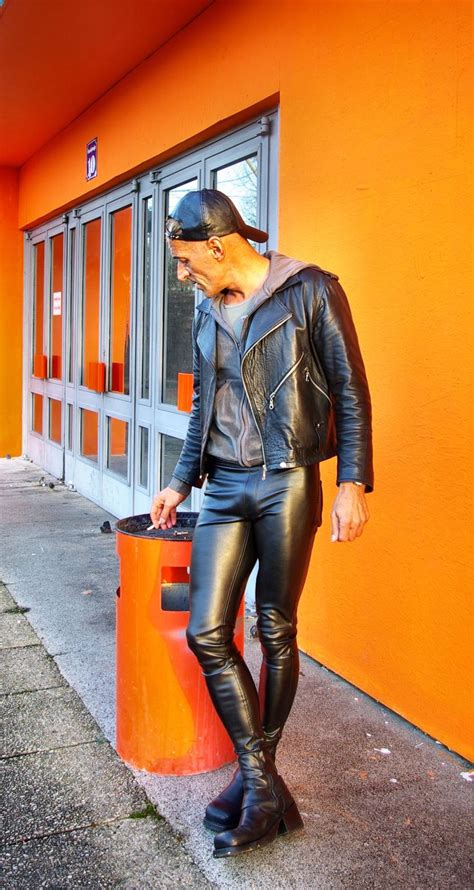 A Man In Black Leather Clothes Standing Next To An Orange Wall