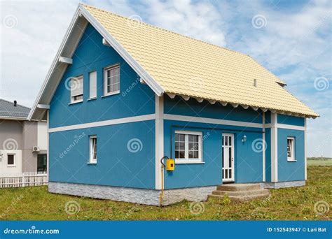 A Small Blue House With White Windows And A Light Yellow Metal Roof