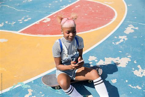 hip girl sitting on skateboard and typing on the phone by stocksy contributor jovo jovanovic