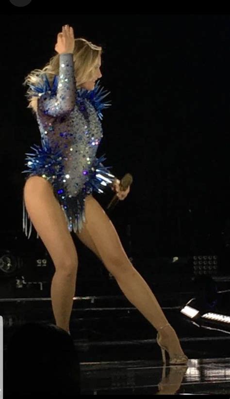 A Woman In A Blue And Silver Outfit On Stage With Her Hands Up To The Air