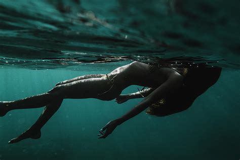 full length dramatic underwater view of a woman in a bikini floating photograph by cavan images