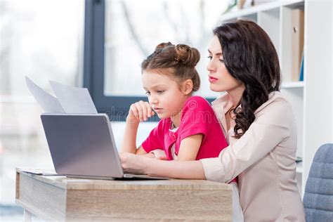 Daughter And Mother Working With Laptop And Looking At Papers In Office