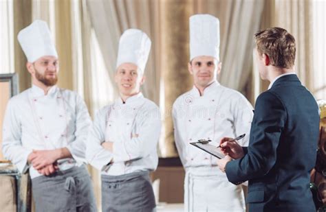 Restaurant Manager And His Staff In Kitchen Interacting To Head Chef