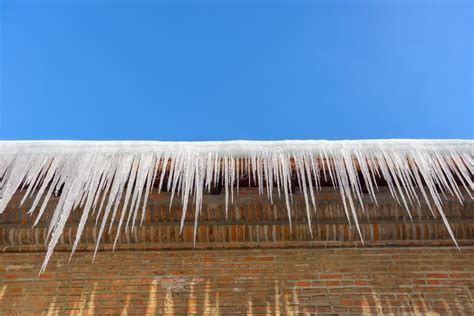 Big Icicles On The Roof Of A Townhouse On A Snowy Winter Day Among Thaw