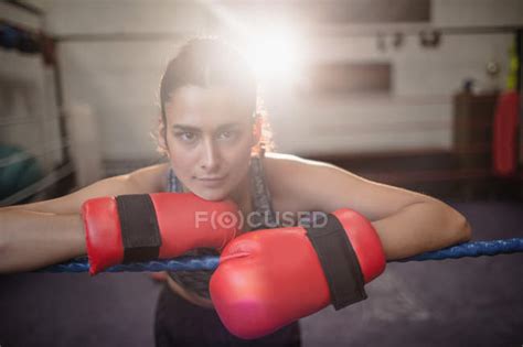Portrait Of Female Boxer In Boxing Gloves Leaning On Boxing Ring Rope