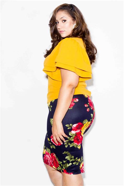 A Woman In Yellow Top And Floral Skirt Posing For The Camera With Her
