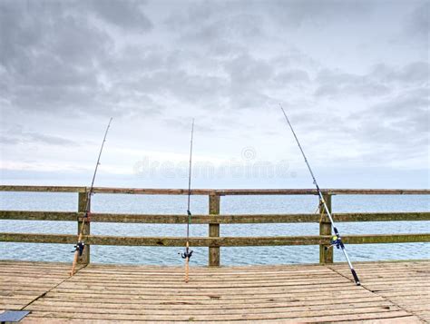 Several Fishing Rods Against The Wooden Railing Of The Beach Pier