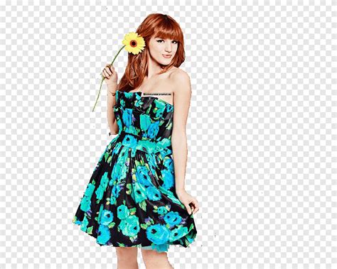 Bella Thorne de pé e sorrindo Bella Thorne em um vestido floral azul e preto segurando uma flor