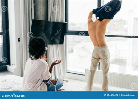 Backside Of Man Taking Off His White Shirt Against Panoramic Window