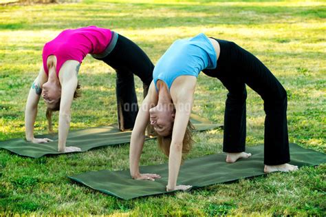 Two Women Bending Over Backwards On Yoga Mats Outdoorsの写真素材