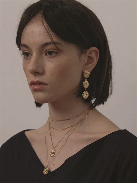 A Woman With Short Hair Wearing Two Necklaces And A Black Top Is