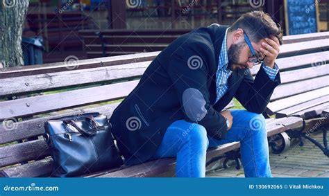 Young Man With Sad Facial Expression Sitting On A Bench In The Park