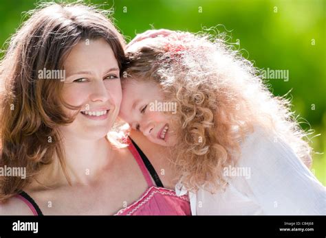 Beautiful And Happy Young Mother Hugging Her Daughter Both Smiling Summer Park In Background