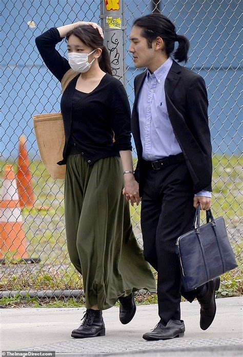 A Man And Woman Walking Down The Street Wearing Masks