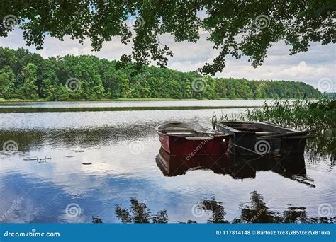 Summer Landscape With Calm Lake And Moored Fishing Boats Under Trees On