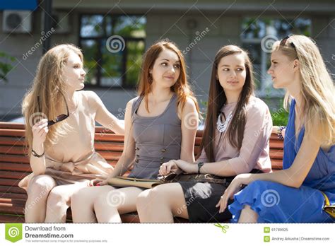 Four Teenage Girls Sitting On Bench In Summer Park Stock