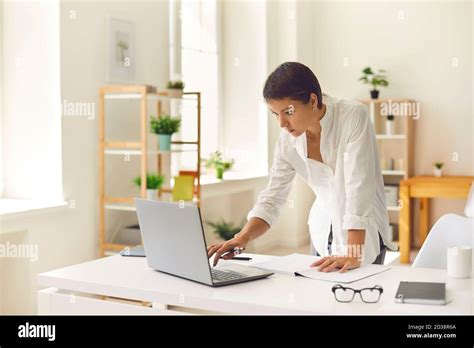 Serious Concentrated Woman Standing At Desk In Home Office And Working