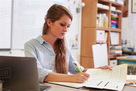 Young Female Teacher At Her Desk Marking Students Work Stock Photo
