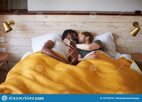 Male Gay Couple Lying In Bed At Home Checking Mobile Phones Together Stock Image - Image of ...