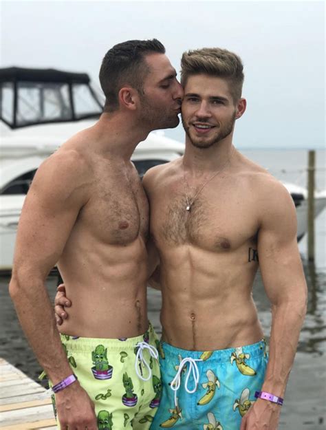 Two Men Standing Next To Each Other On A Dock Near The Water With Boats