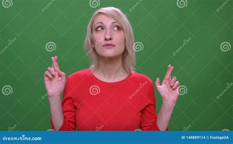 Middle Aged Blonde Short Haired Model Prays With Crossed Fingers Isolated On Green Background