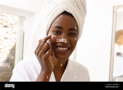 Portrait Of Smiling Young African American Woman Applying Moisturizer On Cheeks In Bathroom