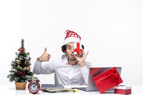 산타 클로스 모자가 그의 얼굴에 그의 선물을 제기하고 흰색 배경에 완벽한 제스처를 만드는 재미있는 비즈니스 사람과 크리스마스 분위기 무료 사진