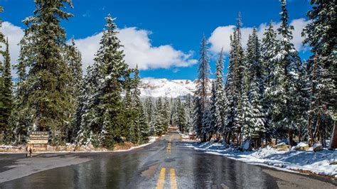 Road Between Snow Covered Trees And Mountains Under White Clouds Blue