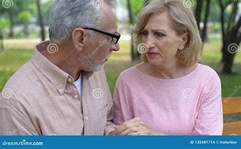 Depressed Senior Woman Looking At Husband Holding Hands Relations