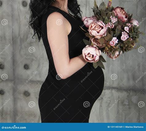 Hands And Belly Of A Pregnant Woman With A Bouquet Of Flowers In Black Clothes Stock Image