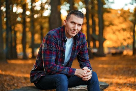 Handsome Smiling Man Sitting On A Bench In The Autumn Park Stock Photo
