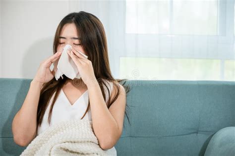 Sick Woman Sitting Under Blanket On Sofa And Sneeze With Tissue Paper