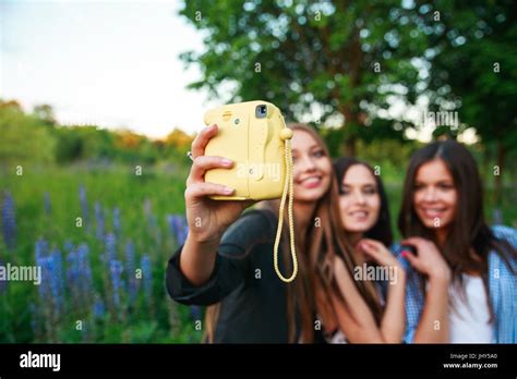 Three Hipsters Girls Blonde And Brunette Taking Self Portrait On Polaroid Camera And Smiling