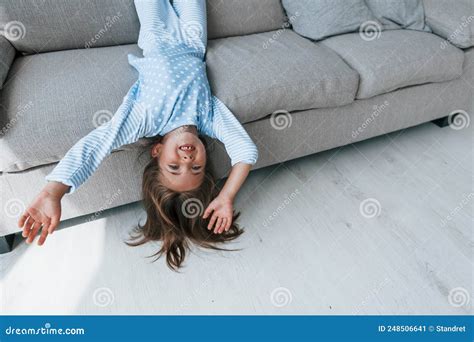 Lying Upside Down On The Sofa Cute Little Girl Indoors At Home Alone