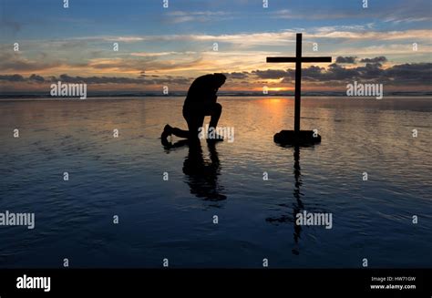 Man Kneeling In Prayer By A Cross On A Beach At Sunset Stock Photo Alamy
