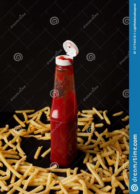Bottle Of Ketchup Surrounded With French Fries Isolated On Black Stock
