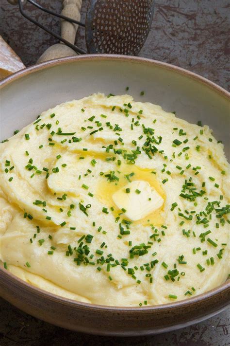 a bowl filled with mashed potatoes topped with butter and chives next to bread