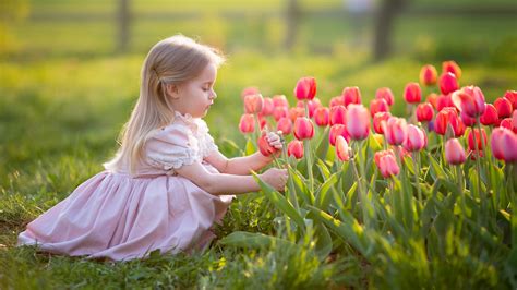 Cute Little Girl Is Touching Tulip Sitting On Grass