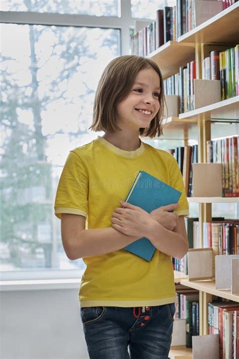 Smiling Happy Schoolgirl Chooses A Book In The School Library The