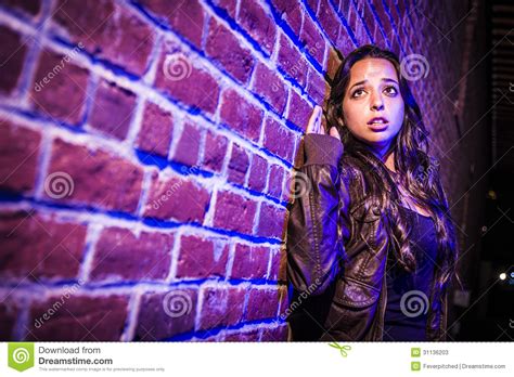 Frightened Pretty Young Woman Against Brick Wall At Night Stock Image