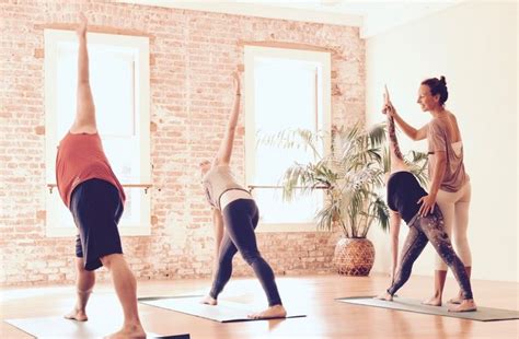 a group of people doing yoga in a room with brick walls and windows on either side of them