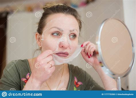 Girl In A Cosmetic Face Mask Looks In The Mirror Stock Photo Image Of