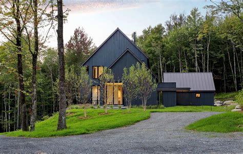 A Black House In The Woods Surrounded By Trees And Grass With A Gravel