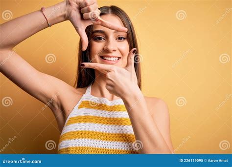 joven y hermosa mujer morena con una camiseta casual a rayas sobre fondo amarillo sonriendo en