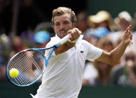 A Man Swinging A Tennis Racquet At A Ball On A Court With People In The