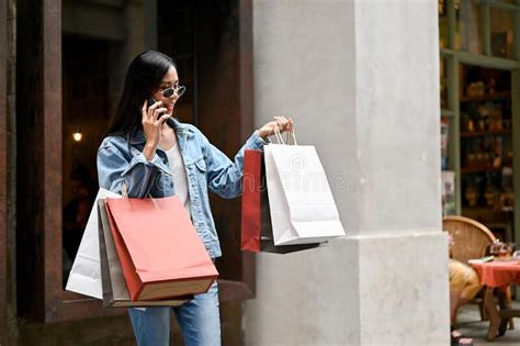 Young Asian Woman Using Smartphone And Carrying Shopping Bags While