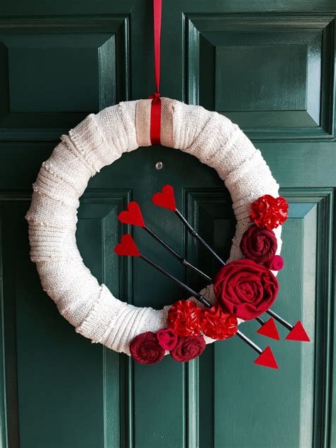 A White Wreath With Red Flowers And Hearts Hanging On The Front Door