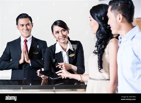 Workers Are Welcoming Young Couple At Hotel Reception Area Stock Photo