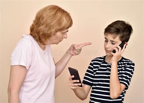 Angry Mother Scolding Her Smiling Son With Two Smartphones Stock Photo